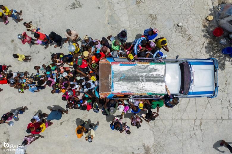 مردم در اطراف خودرویی جمع می شوند که داوطلبان در پناهگاهی برای خانواده هایی که در اثر خشونت گروهی آواره شده اند در کلیسای سنت ایو در پورتو پرنس ، هائیتی غذا به پناهندگان تقسیم می کنند ، 26 ژوئیه 2021