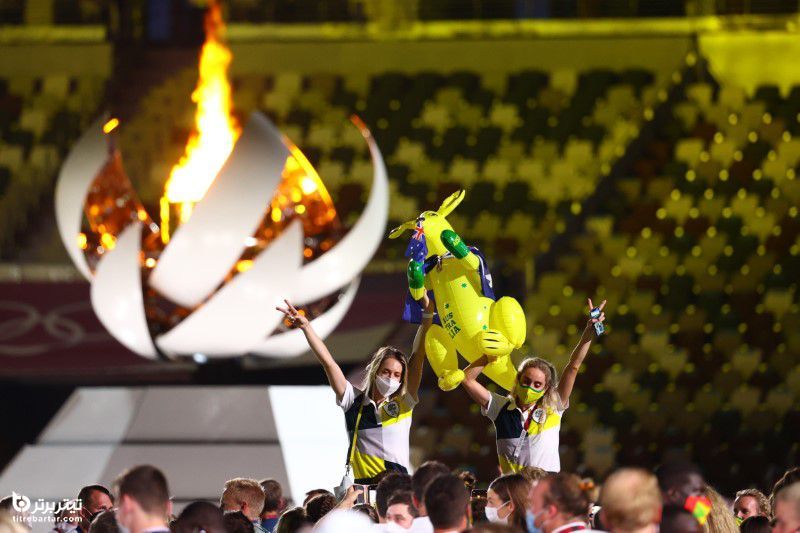اعضای تیم استرالیایی یک طلسم بادی در مقابل مشعل المپیک در دست دارند