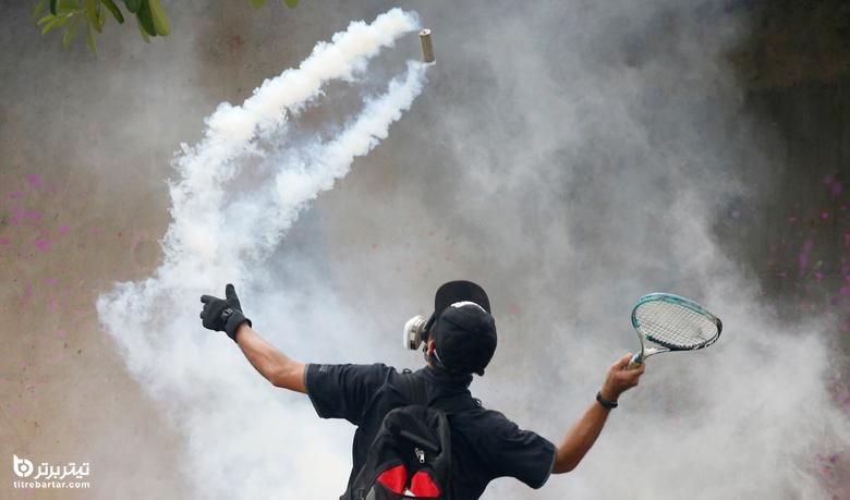 یک تظاهرکننده در اعتراض به برخورد دولت با همه گیری ویروس کرونا ، در بانکوک ، تایلند از یک راکت علیه یک قوطی گاز اشک آور استفاده می کند