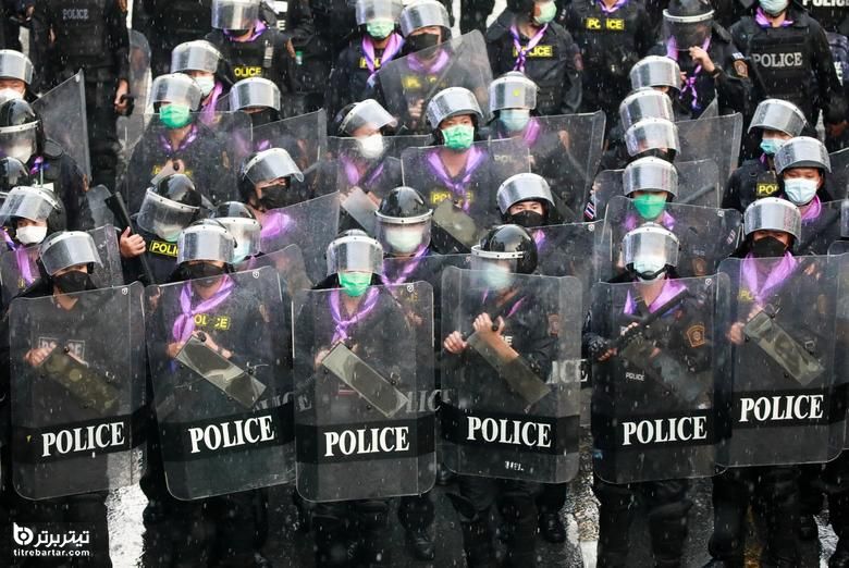 مأموران پلیس در اعتراض به نحوه برخورد دولت با شیوع ویروس کرونا در نزدیکی دفتر پلیس در بانکوک ، تایلند ، زیر باران نگهبانی می کنند.