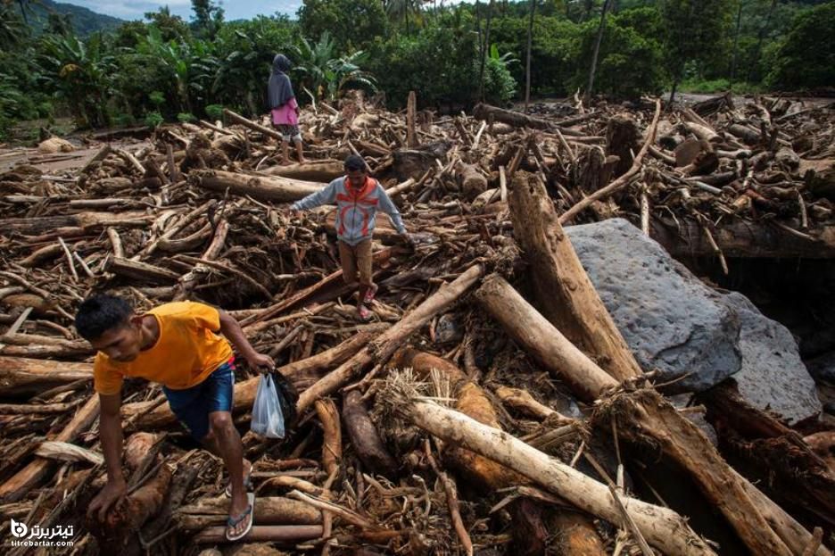 مردم پس از جاری شدن سیل در اثر طوفان در اندونزی ، از میان انبوهی از تنه درختان عبور می کنند