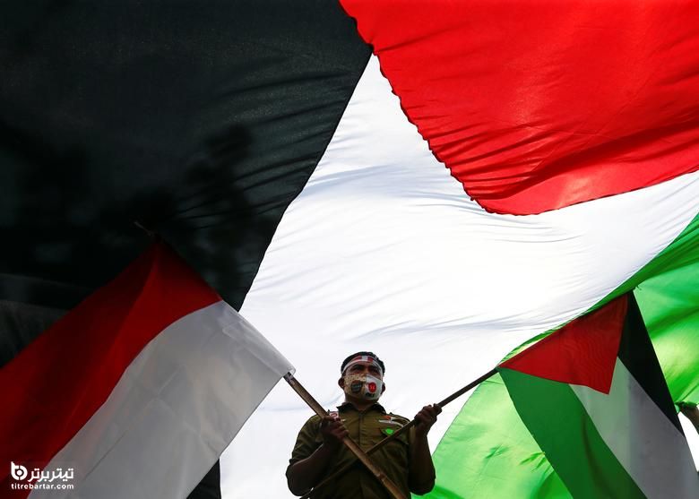 یک معترض اندونزیایی زیر پرچم بزرگ فلسطین در هنگام اعتراض به حملات ضد اسرائیلی