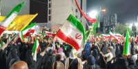 عکس | تصویری جالب از حضور یک زن در تجمع شبانه تهران با طوطی سبز با پرچم جمهوری اسلامی ایران